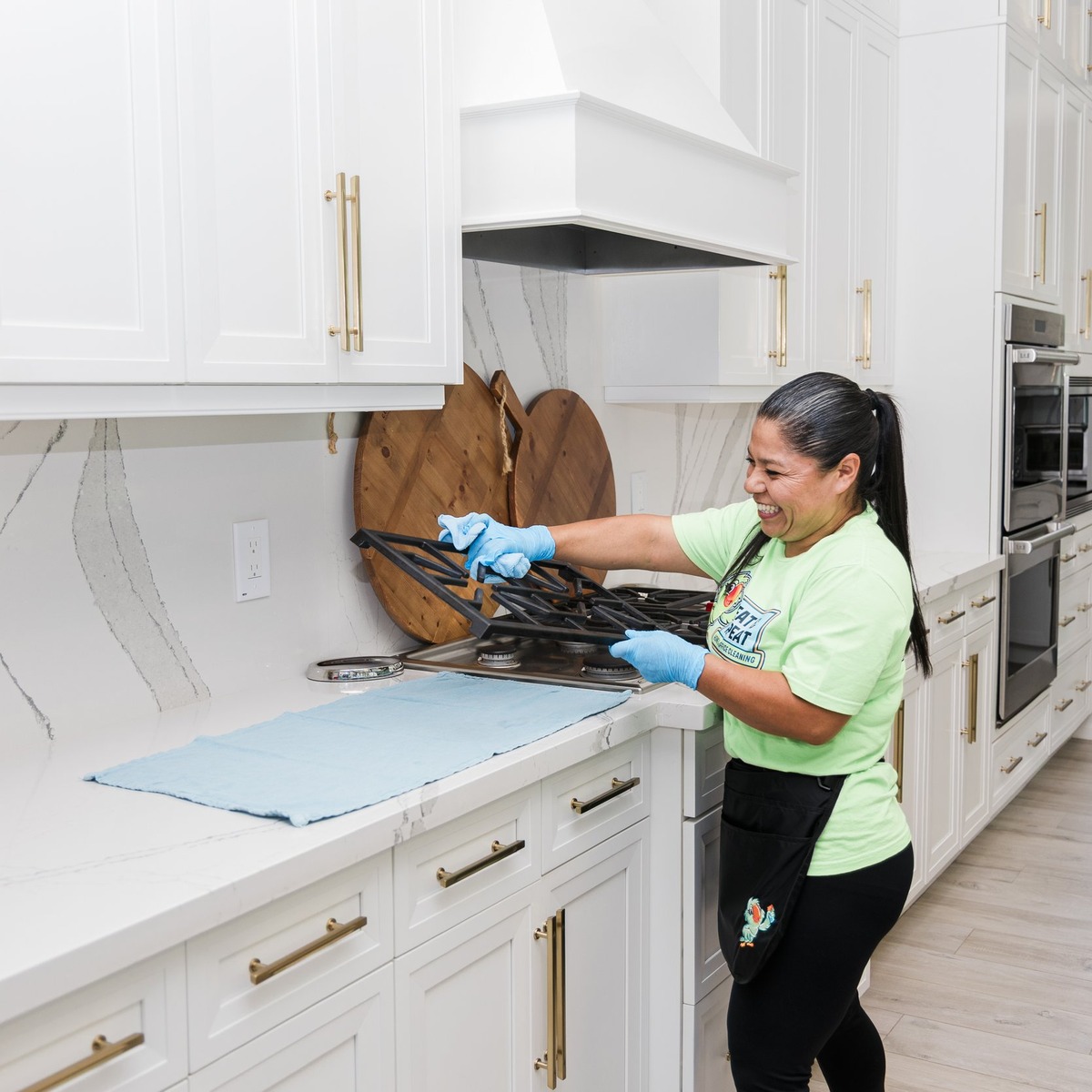 Professional cleaner handling stovetop grates while cleaning a bright residential kitchen as part of weekly cleaning services near me.